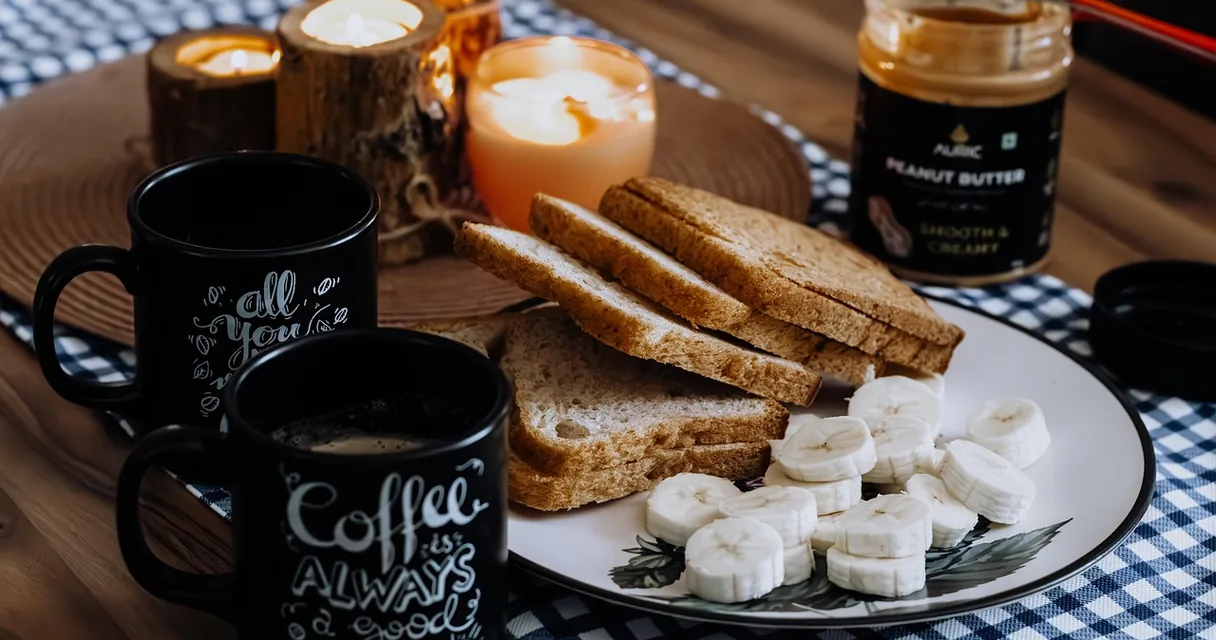 Mesa de café da manhã com torradas integrais, banana fatiada e canecas de café